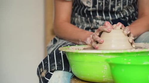 A female potter works on a potter's wheel, making a ceramic pot from clay in a pottery workshop
