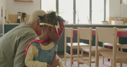 Woman Lifts Child in Superhero Costume in Kitchen