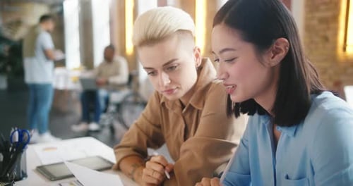Women Do Paperwork Sitting at Table Against Men in Office