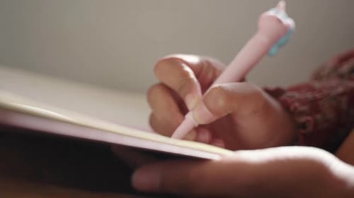 Close up of a young females hand writing on a pad of paper while sitting on public transport. Hand h