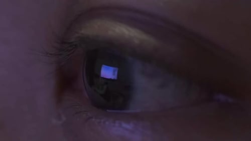 close up of female eye blinking, television screen reflected in eye