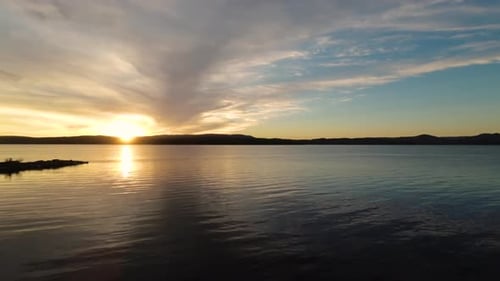 Scenic aerial view flying over a lake toward a picturesque summer sunset.