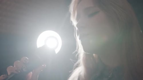 A Young Woman Recording a Song in the Studio Singing in the Mic with Bright Back Lighting Behind Her