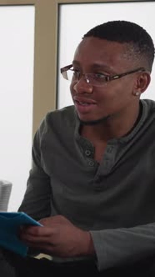 Black Man with Book Sits on Floor Indoors