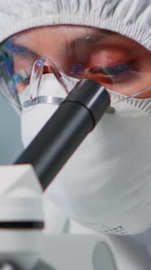 Researcher in Protective Suit Looks Through Microscope