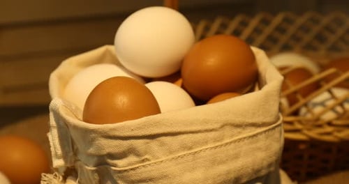 Woman putting raw chicken eggs from sack into basket at table, closeup