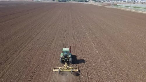 Green Tractor cultivating and seeding a dry field - Top down aerial footage