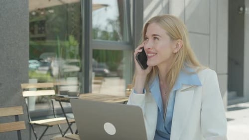 Smiling Businesswoman Talking On Smartphone At Outdoor Cafe Workspace