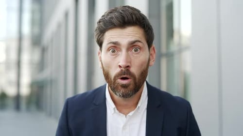 Close up of amazed happy businessman looking surprised at camera standing on street near office