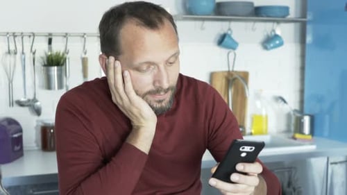 Man Using Smartphone Then Looking at Camera in Kitchen