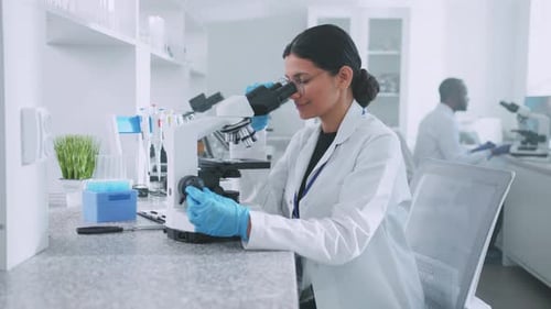 Wissenschaftlerin mit Schutzhandschuhen schaut unters Mikroskop Arbeiterin im Labor
