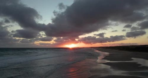 Sunset at the beach with dramatic clouds reflecting the warm glow of the sun, waves gently lapping t
