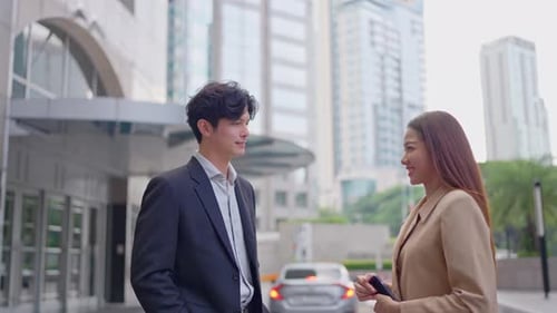 Asian businessman and businesswoman making handshake outdoors in city.