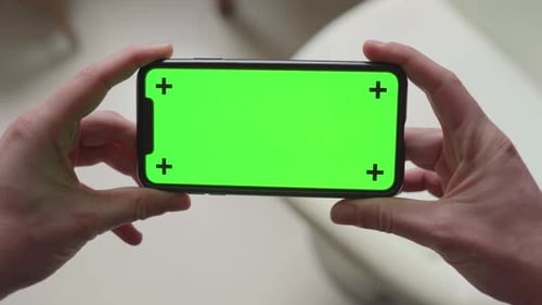 two hands holding smartphone with green screen display and tracking markers, changing orientation fr