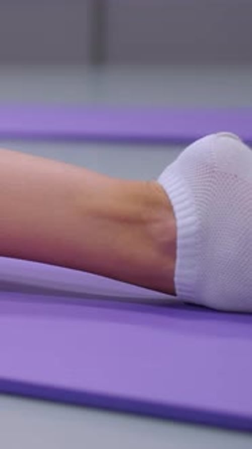 Woman stretching ankle on purple yoga mat indoors
