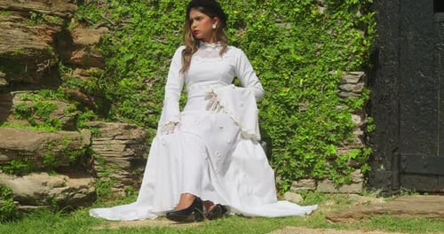 A girl adorned in a vintage bridal dress standing gracefully in the courtyard of a fort.
