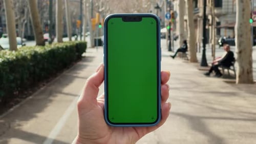 Female Hand Holding Smartphone with Mockup Green Screen in the European City Concept of Chroma Key