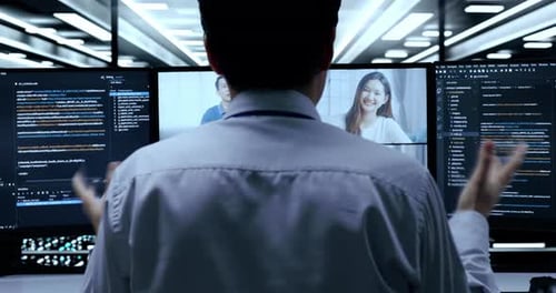 Asian Male Programmer Having A Meeting While Writing Code By Desktops Using Multiple Monitors