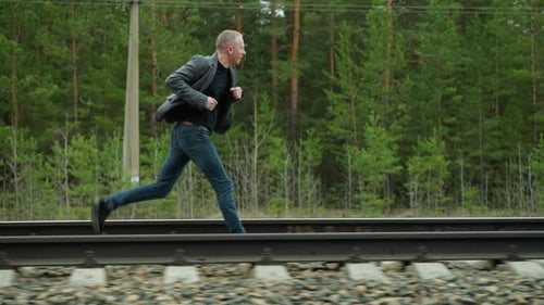 Man in Grey Suit Running on Railway Tracks in Forest