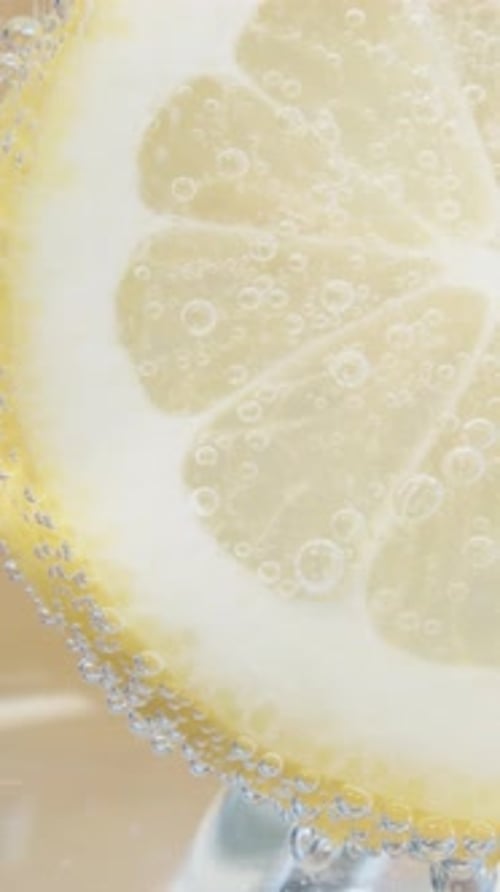A slice of lemon in a glass of lemonade. Close-up bubbles. Vertical video Social Media. Slider