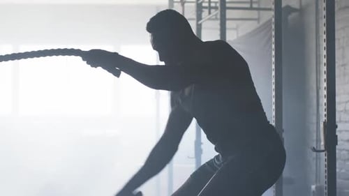 Exercising with battle ropes, man training in gym for strength and endurance