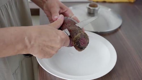 Woman Peels Fresh Beetroot with Knife in Kitchen