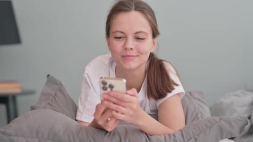 Woman Using Smartphone While Lying on Gray Bed