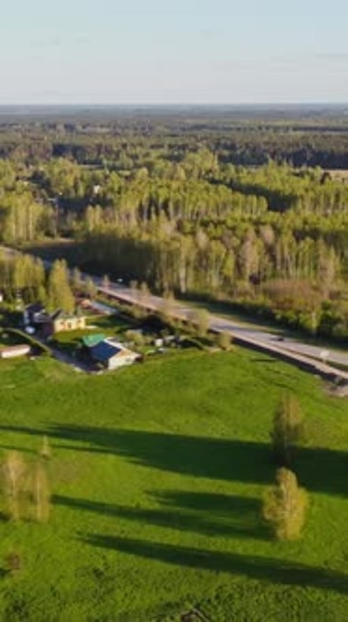 Vertical slow drone pull away over Katlakalns spring countryside, showing traffic and houses
