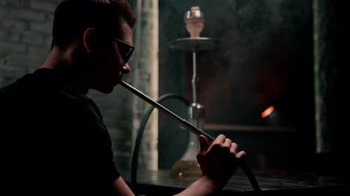 Hookah man in glasses smoking a traditional hookah pipe Man exhaling smoke in a hookah cafe or bar
