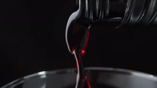 I pour red wine into a glass, on a black background. Dolly slider extreme close-up.