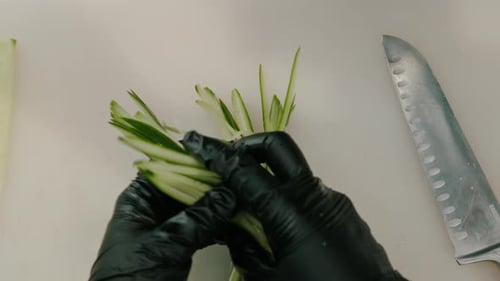 Close-up of a sushi maker in gloves cutting a cucumber with a professional kitchen knife on a board