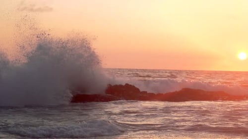 Super slow motion waves crashing on reef in front of sunset in California on summer night