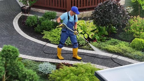 Gardener Using a Pressure Washer to Clean Outdoor Stone Paths in a Landscaped Garden