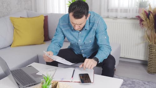 Man looking at bills at home calculating with calculator.