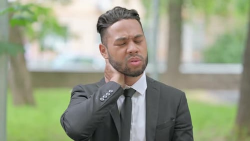 Young Adult Man Rubs Aching Neck in Park
