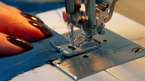 Primer plano en un taller de costura con una máquina que la maestra costurera hace un corte sobre una tela azul