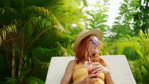 Redhead Woman Relaxes By Poolside Sipping Watermelon Cocktail in Sun Sunglasses Leisure in Tropical