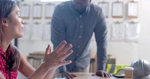 Happy diverse male and female architects discussing blueprints on table in office, slow motion