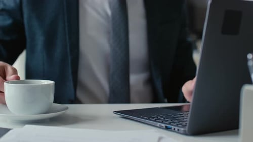 Man Types on Laptop with Coffee Cup Nearby