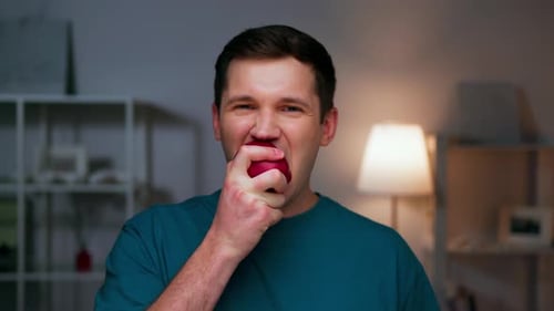 Young Adult Man Bites into a Red Apple