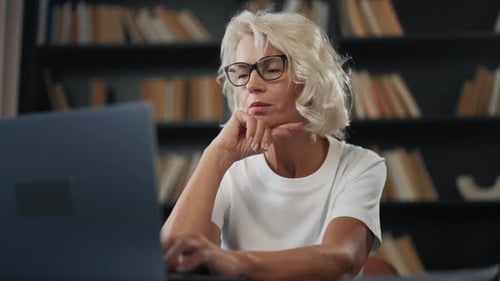 Senior Woman Freelancer Works on Laptop Mature Gray Haired Female in Glasses Working at Home Office