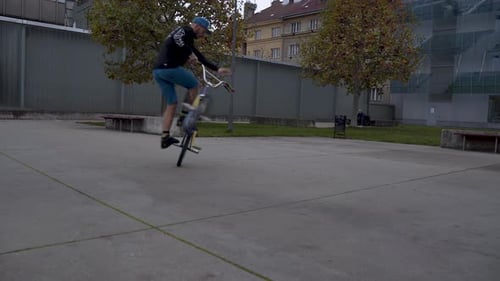 Guy riding a BMX bike, performing the Peg Manual trick in a skatepark.