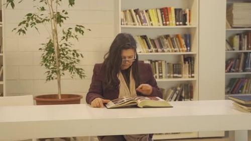 Mature woman reading big book in library. Handheld