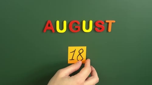 Hand sticking a sticker 18 August calendar day on school board. 18 date of august. Eighteenth day