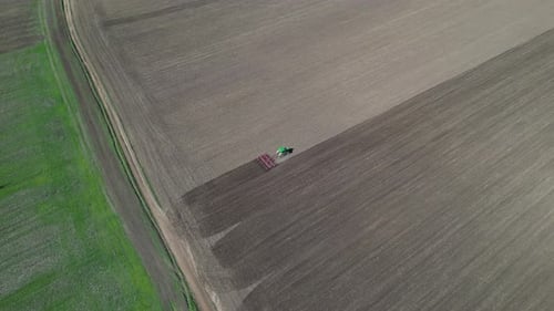 Aerial View of a Tractor Plowing a Large Field Creating Distinct Patterns in the Soil Agricultural