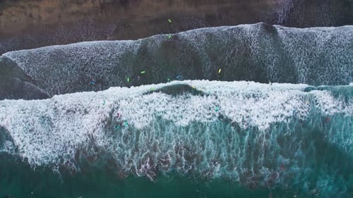 Surfers on colorful boards riding the waves in an ocean, top down aerial view