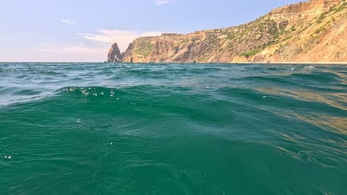 Sea Water Surface Camera Flies Over the Calm Azure Sea with Volcanic Rocky Shores on Background