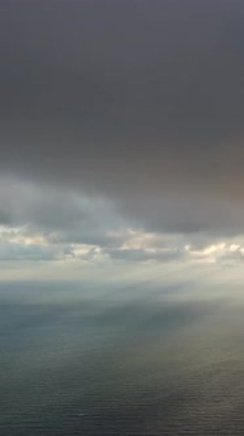 Vertikale Luftaufnahme: Sonnenstrahlen durchbrechen Dramatisch, stimmungsvolle und düstere Regenwolken über dem Meer