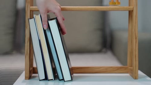 Women's Hand Takes a Book From the Wooden Bookshelf