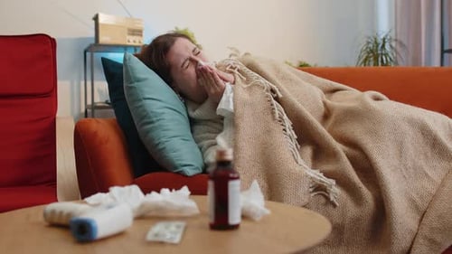Une femme malade souffrant de rhume ou d'allergie, assise sur le canapé de la maison, éternue avec de la morve